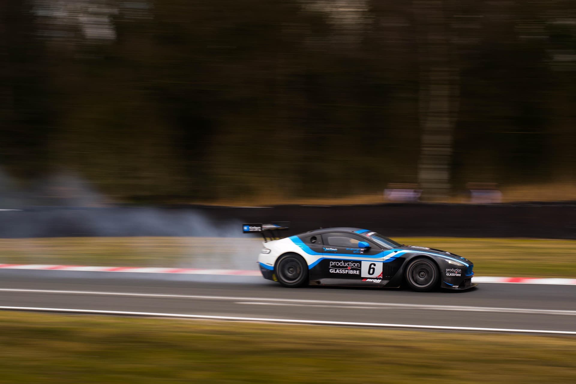 Black, white, and blue Aston Martin V12 Vantage GT3 race car at speed, background blurred by the panning shot