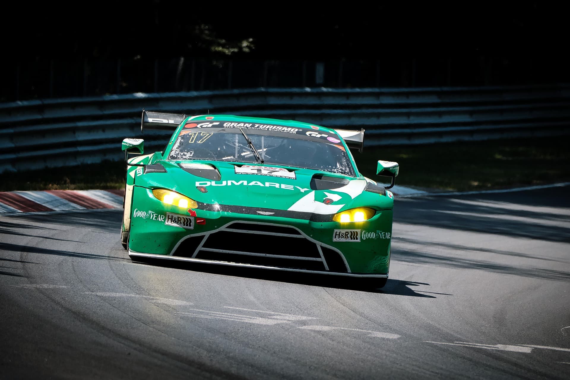 Green Aston Martin Vantage GT3 race car head-on through a corner, headlights lit