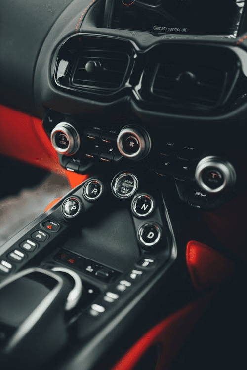 Aston Martin Vantage centre console in low light, showing the PRND transmission buttons, engine start control, and red leather trim