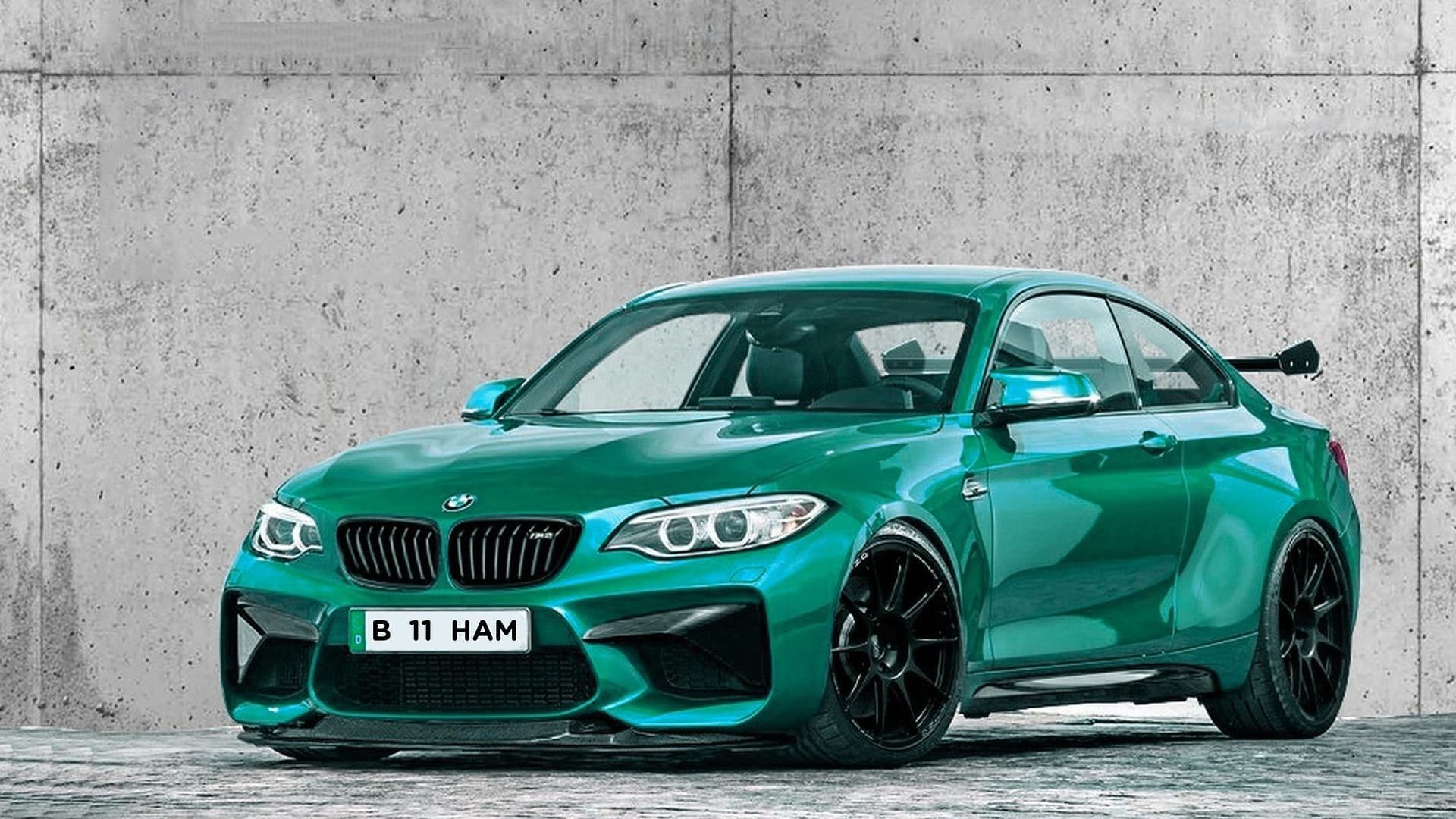 Green BMW M2 coupé with black wheels and a rear wing in front of a raw concrete wall