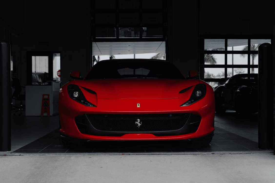 Red Ferrari 812 Superfast facing forward in a dark dealership service bay, framed by the open roller door