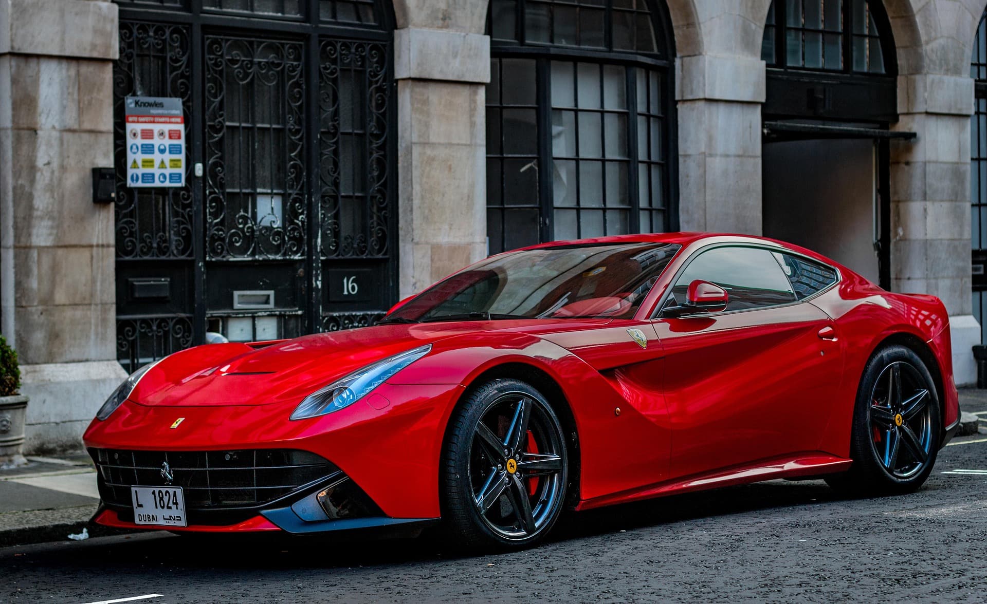 Red Ferrari F12berlinetta on Dubai plates parked outside a stone-fronted London building