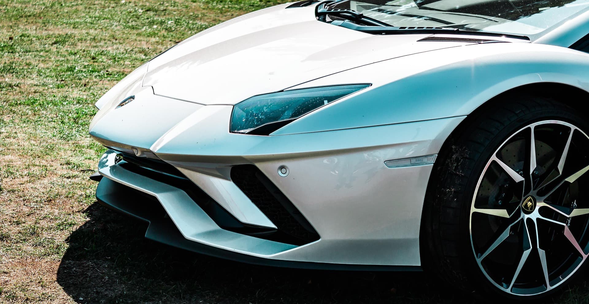 Front corner of a white Lamborghini Aventador S on grass, showing the headlight and front splitter