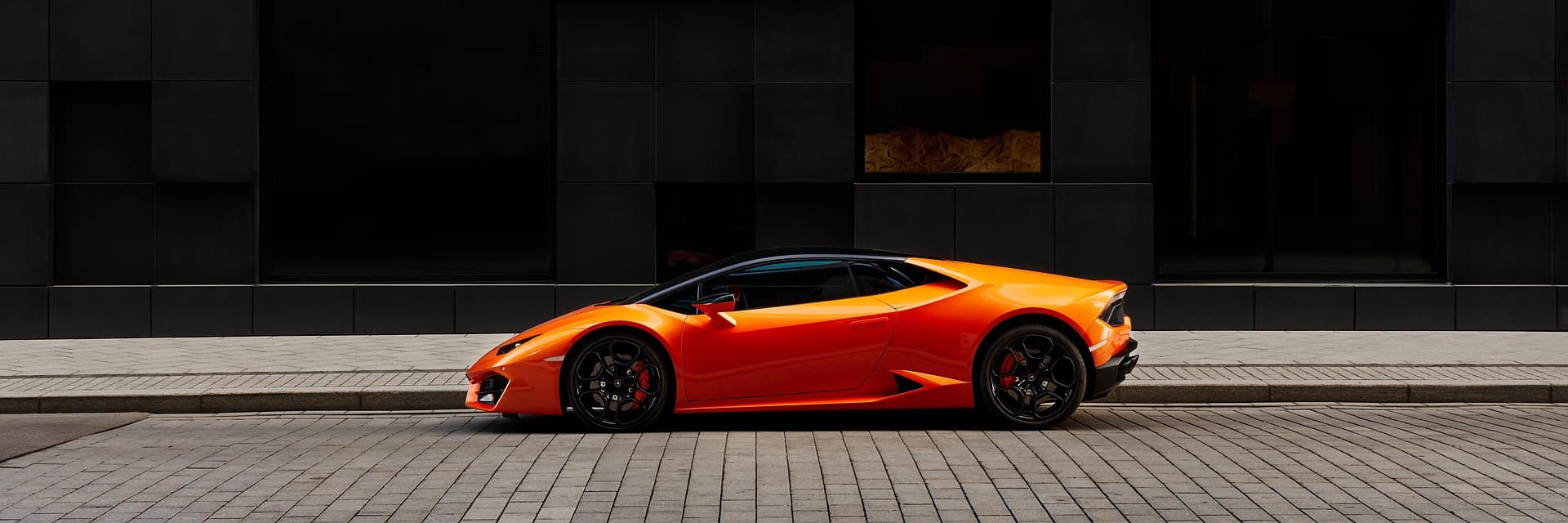Orange Lamborghini Huracán in side profile against a black stone building façade