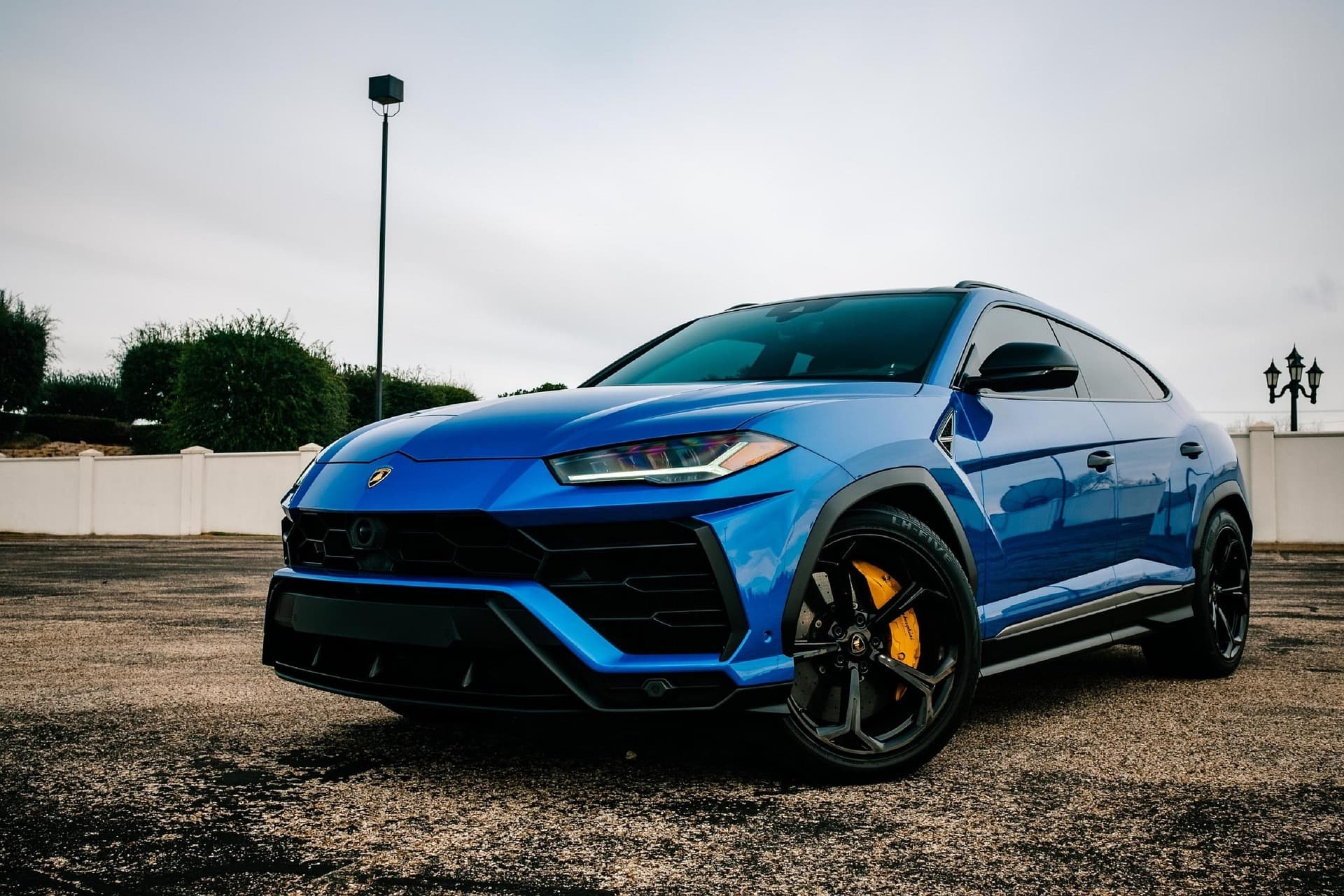 Blue Lamborghini Urus with yellow brake calipers parked on gravel in front of a white wall
