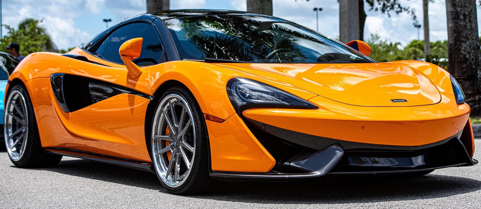 Orange McLaren 570S front three-quarter on aftermarket wheels under palm trees