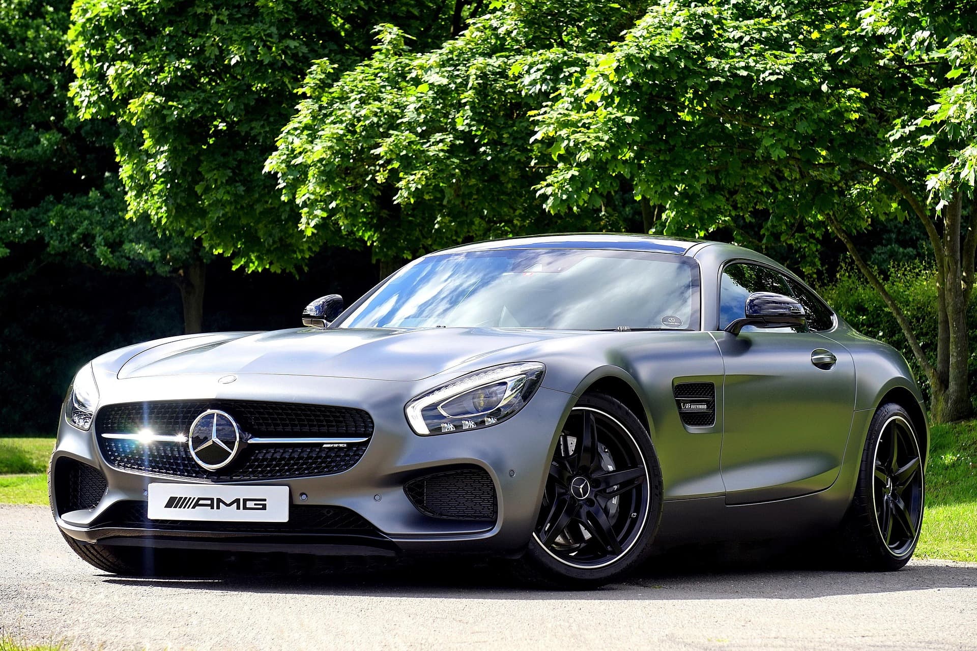 Matte grey Mercedes-AMG GT coupé with an AMG plate parked on a lane beneath green trees