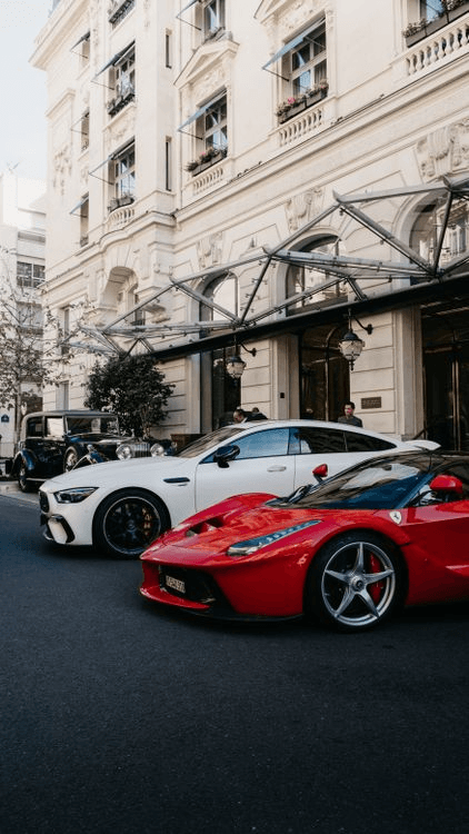 White Mercedes-AMG GT 4-Door Coupé and red Ferrari LaFerrari parked outside a grand hotel entrance on a city street