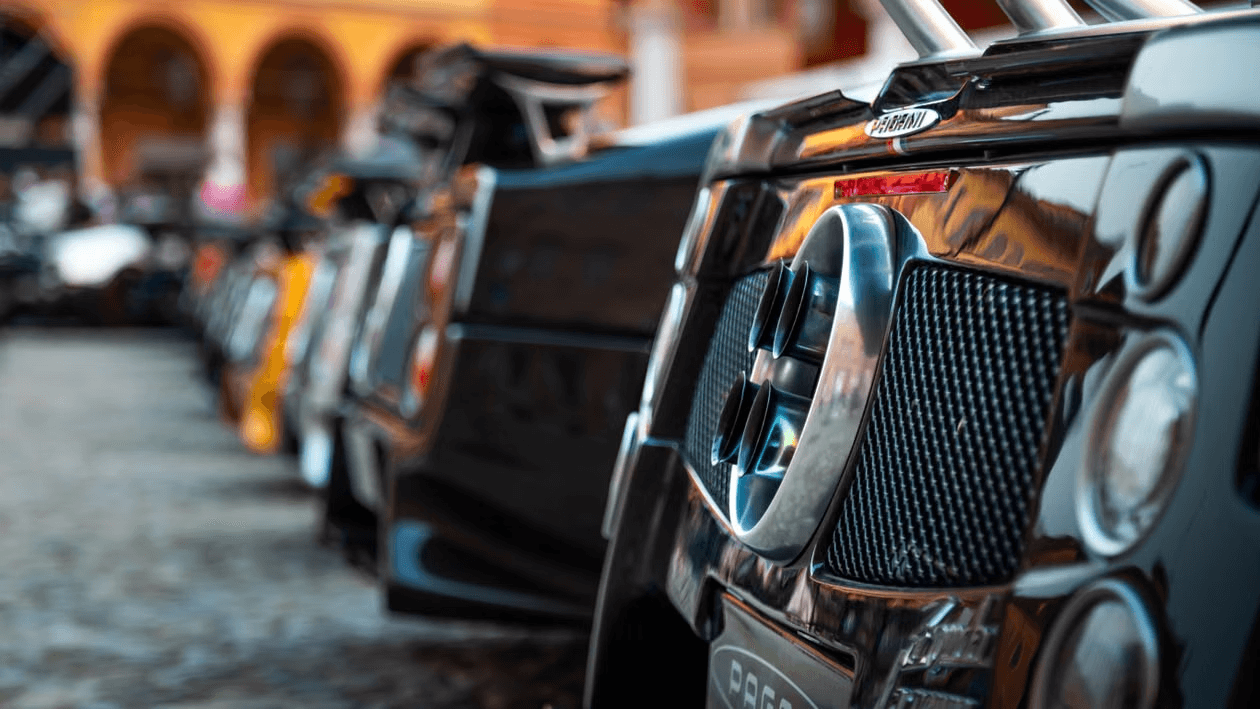 Rear detail of a carbon-bodied Pagani Zonda in a cobbled Italian piazza, with a line of further Paganis fading into the background